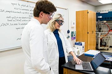 两个穿着实验室工作服，戴着护目镜的人看着电脑